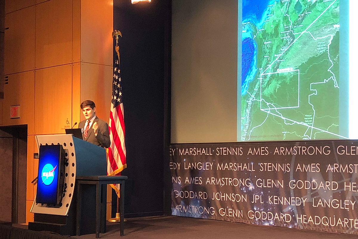 Theurer delivers a presentation about his NASA DEVELOP internship work studying deforestation in Colombia with satellite images onstage at a showcase.