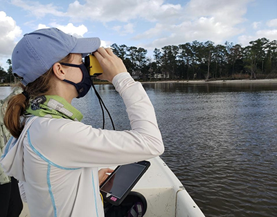 Jessica Richter measures the distance from vessel to shore using a laser rangefinder, to verify the location of survey coordinates along the shoreline of the Neuse River Estuary.