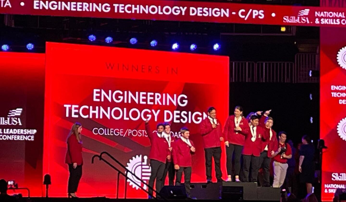 Students standing on a stage with their medals. In the background, a projection says "Engineering technology and design"