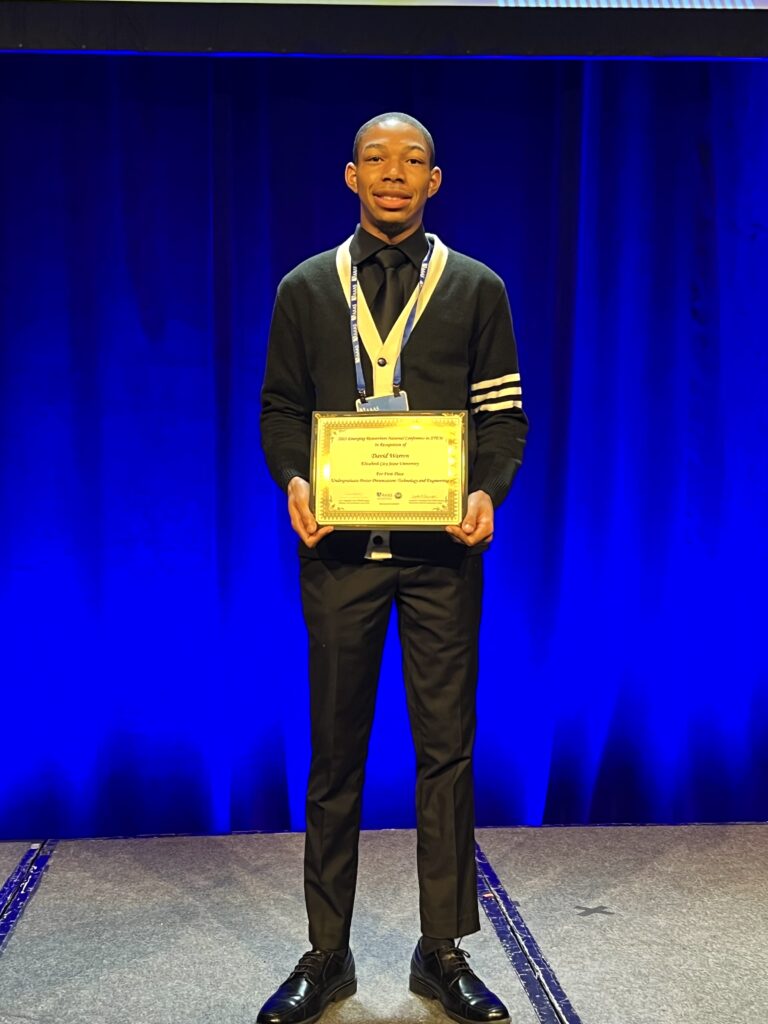 Student stands in front of blue curtain holding an award.