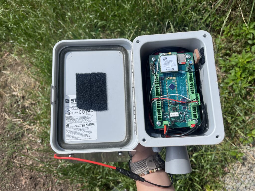 A hand holds a depth sensor node with the top of it off, showing the inside with a wires and a circuit