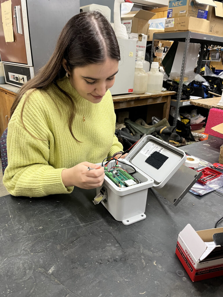 A woman sitting at a table and putting together what is a depth sensor node, an electronic part of the RTC system.