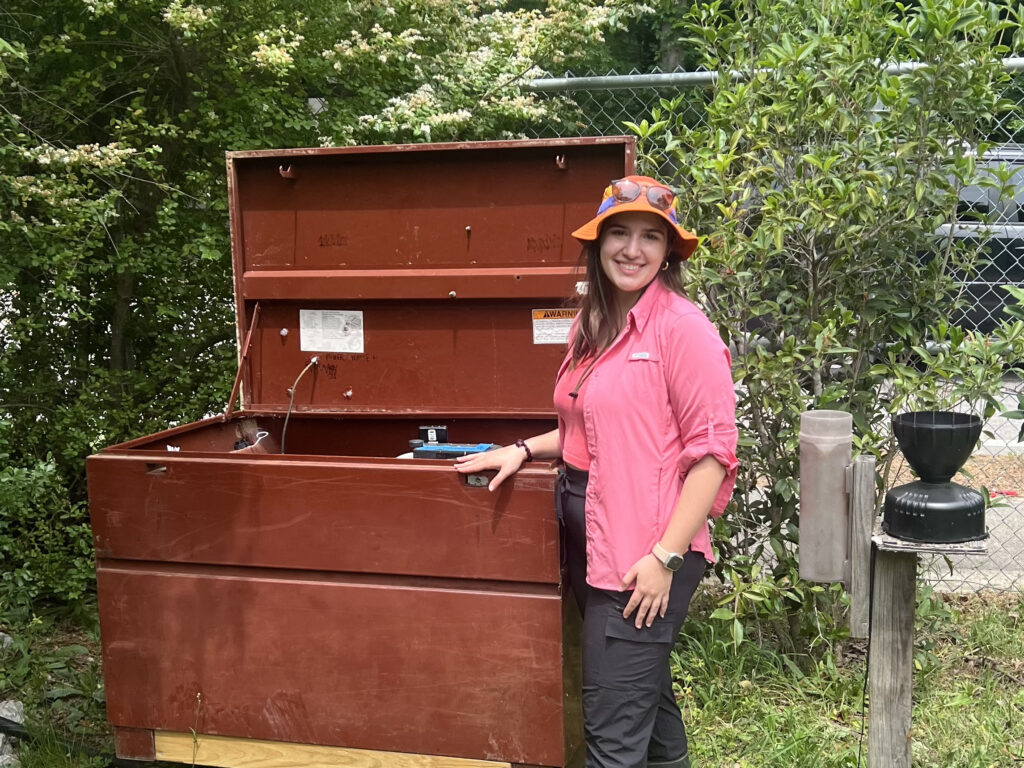 A woman standing next to a water sampler box, which is large and looks like a dumpster