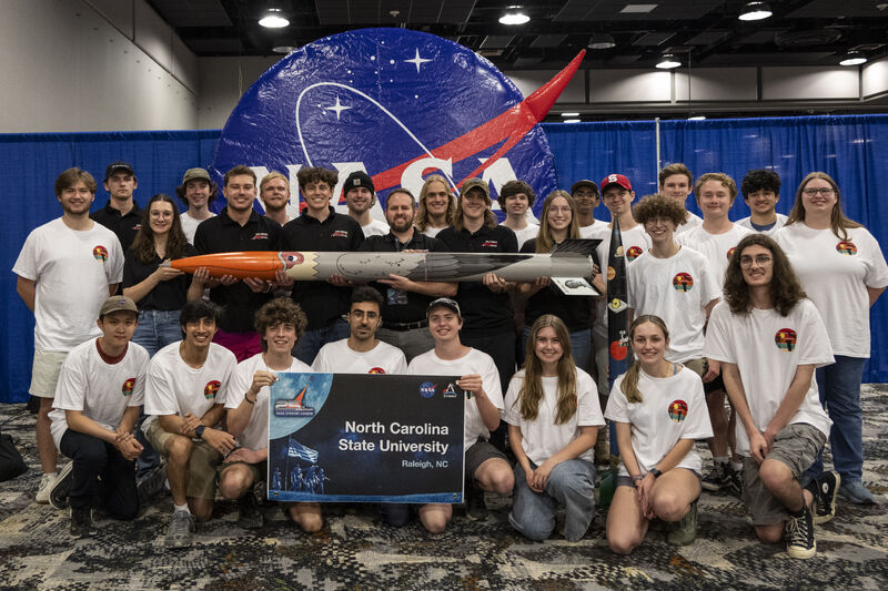 Group of students kneeling in two rows. Blue NASA logo behind them.