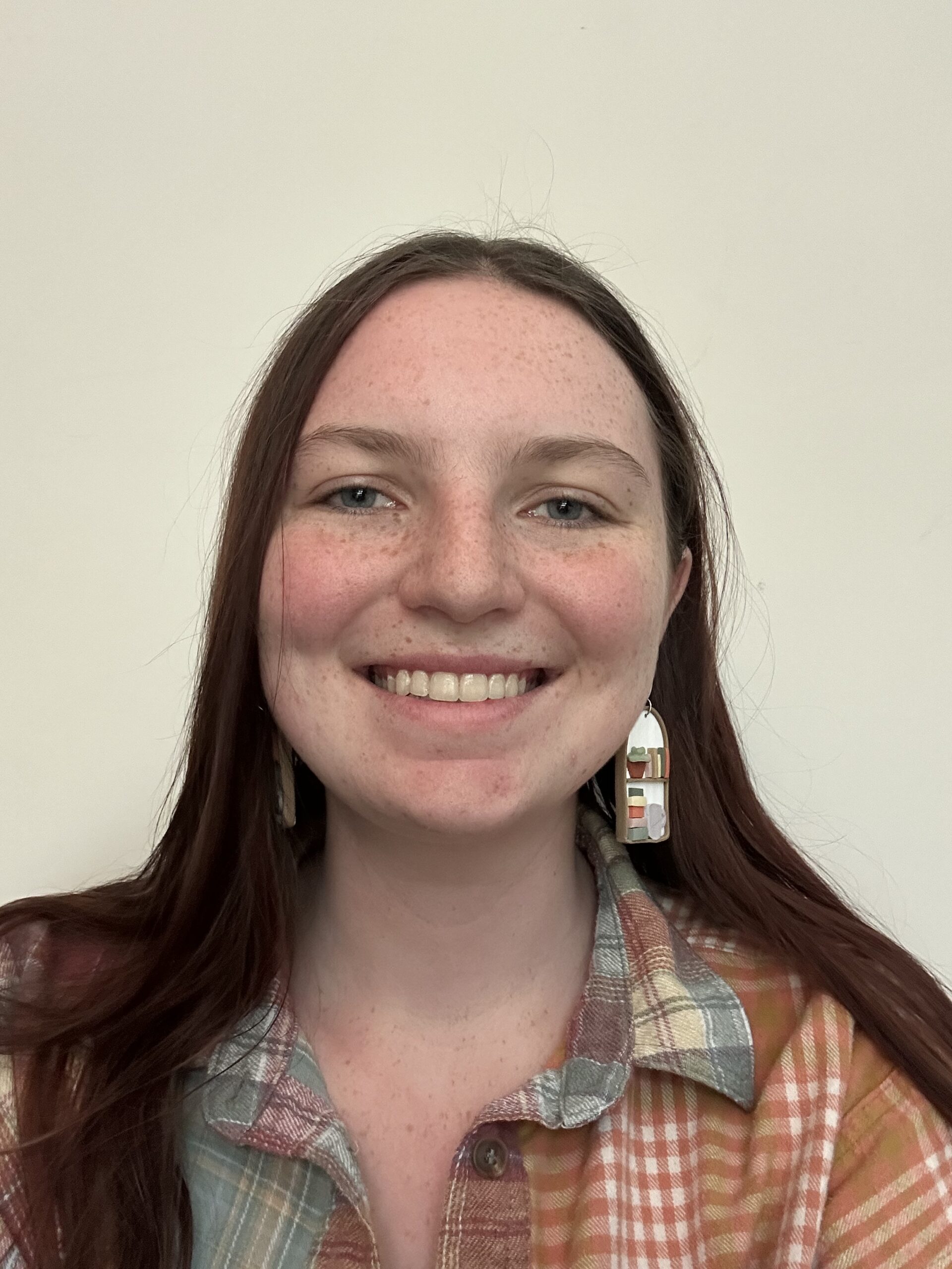 Woman smiles and poses for headshot against a wall.