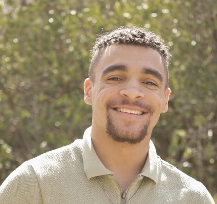 Man smiles and poses for headshot against a wall.