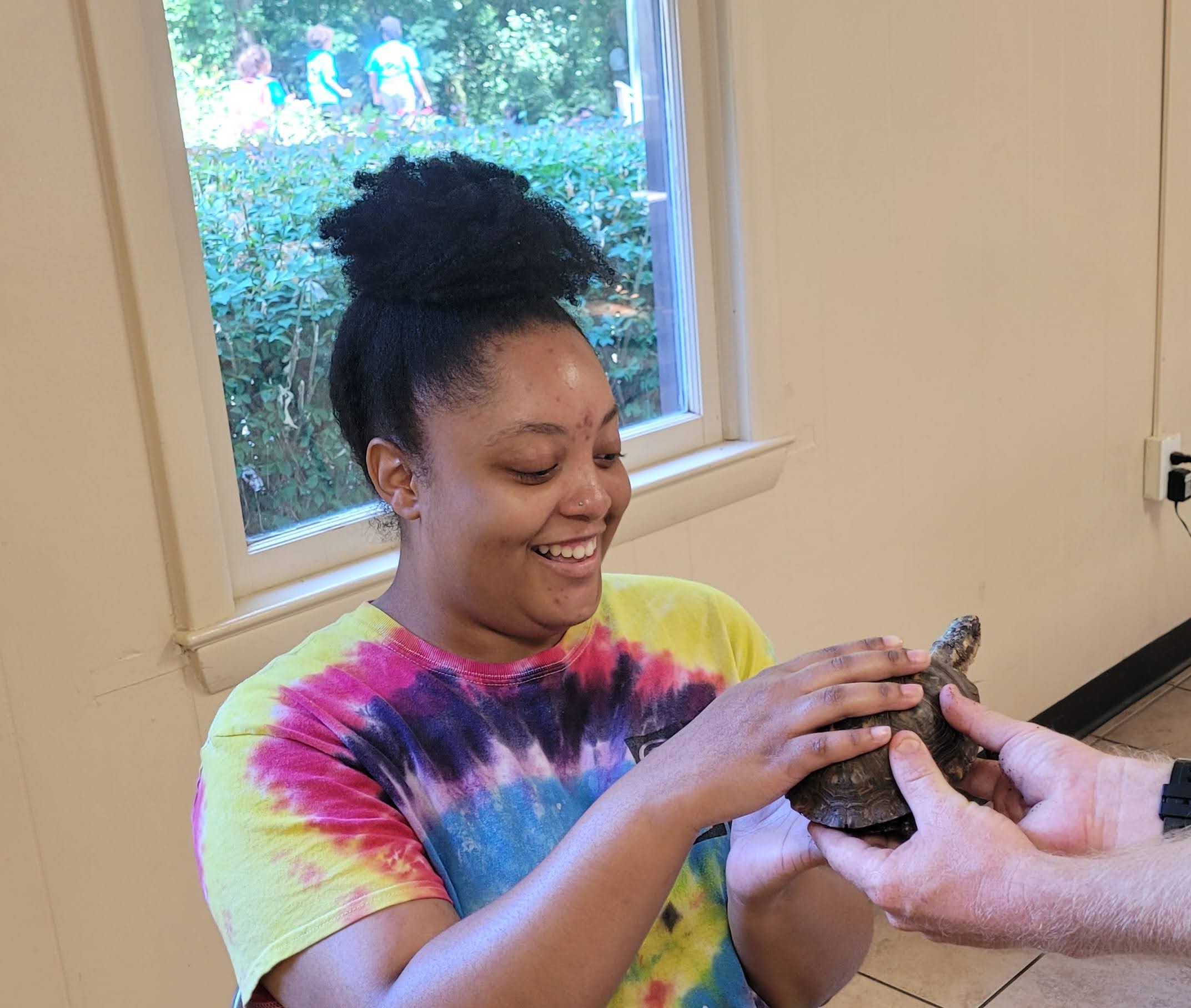 A young woman is touching a turtle that is being held out to her.