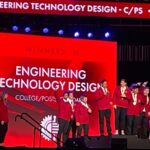 Students standing on a stage with their medals. In the background, a projection says "Engineering technology and design"