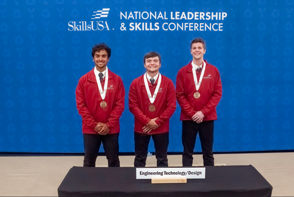 Three young men standing in a line with bronze medals around their necks. The background behind them says "SkillsUSA National Leadership & Skills Conference". A plaque at their feet reads "Engineering Technology/Design"