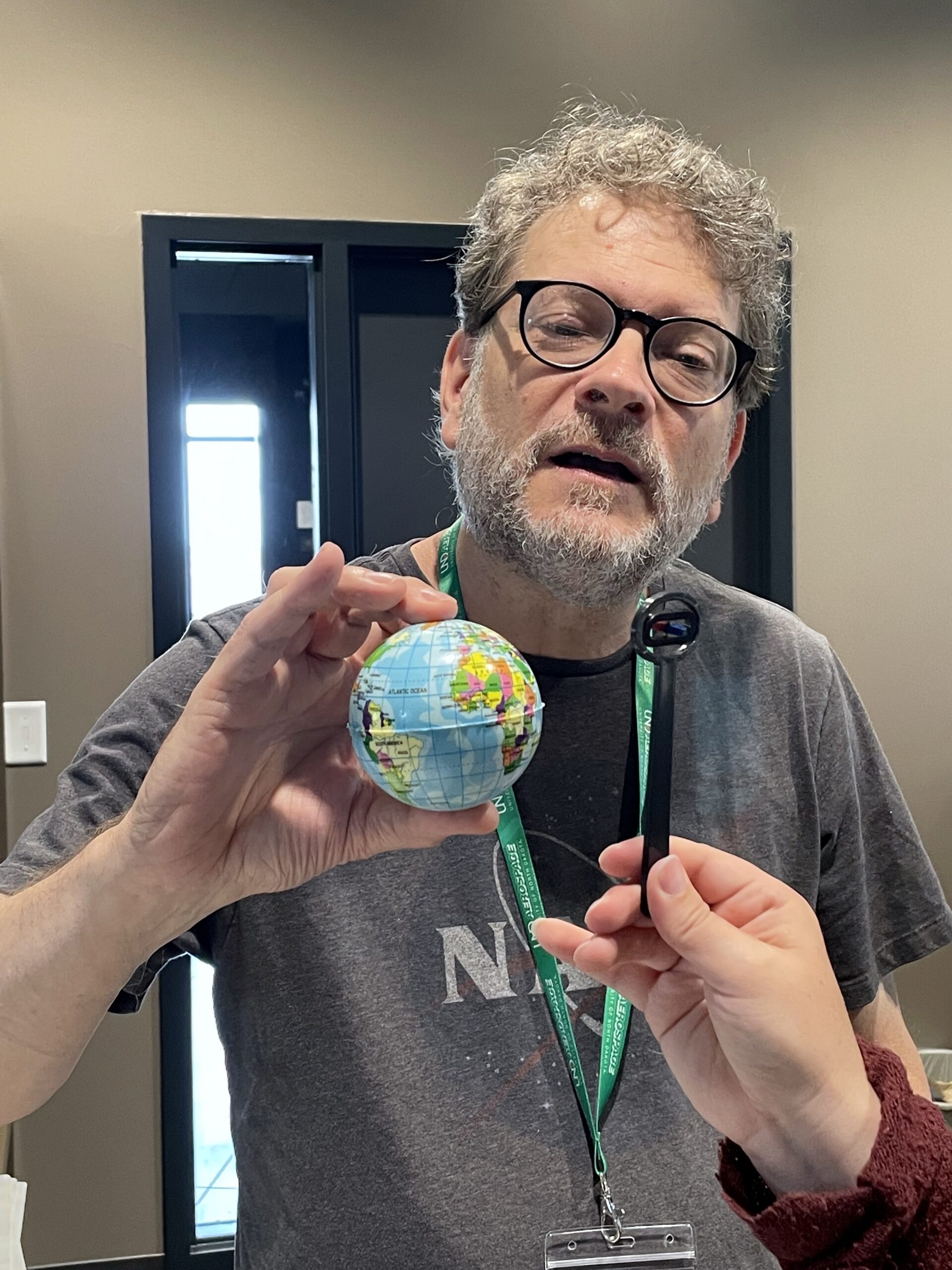 Man holding up a small globe while someone holds a stick up to it.